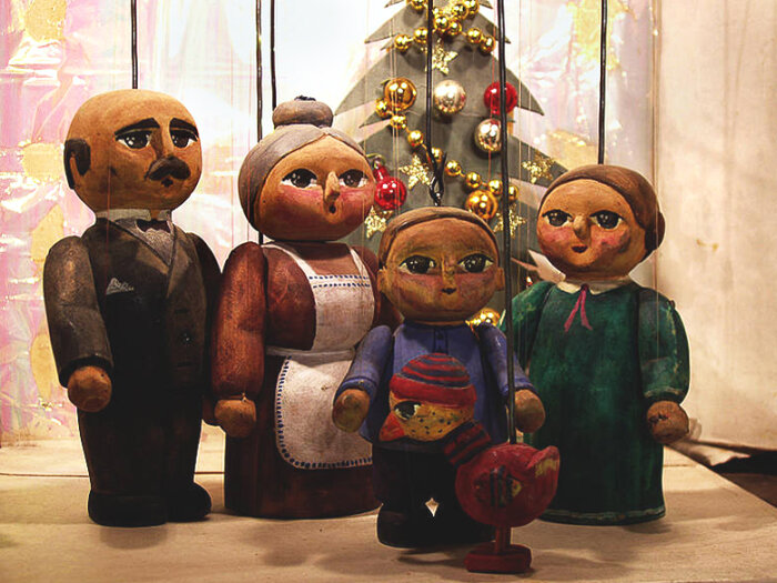 Verschiedene Puppen aus Holz mit einem Weihnachtsbaum aus Holz im Hintergrund