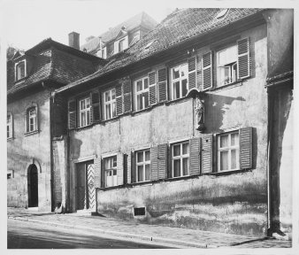 Schwarz-Weiß-Foto eines Hauses mit Fensterläden an einer Bergstraße.