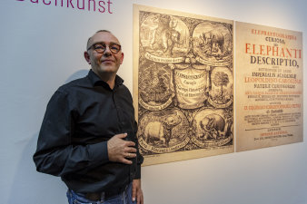 Bild: Carsten Berndt in der Ausstellung „Elephantographia Curiosa. Der Erfurter Kupferstecher Jacob Petrus und sein Beitrag zur barocken Buchkunst“ © Stadtverwaltung Erfurt Ein Mann steht vor einer großen Tafel in einer Ausstellung