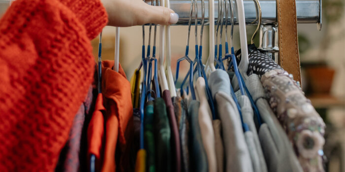 eine Hand befindet sich an einer Kleiderstand, an der viele Kleiderbügel mit Kleidung hängen