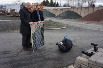 Drei Männer halten ein Bild, davor liegt ein Fotograf
