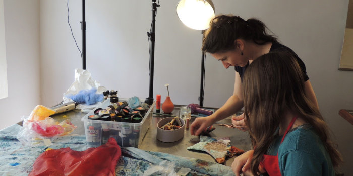 eine Frau und ein Mädchen arbeiten an einem Tisch künsterlisch mit Stoff
