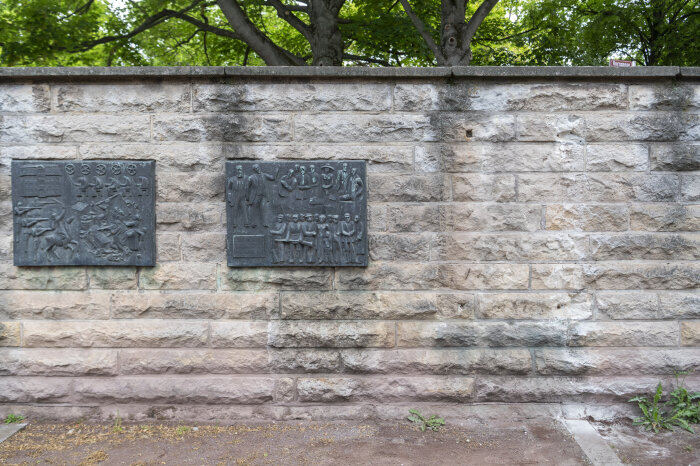 ein einer Mauer hängen zwei dunkle Platten mit erhabenen Motiven