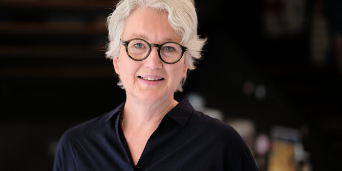 Porträtaufnahme von einer Frau mit Brille vor einem dunklen Hintergrund