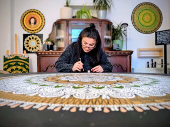 Eine Frau mit dunklen Haaren und Brille malt ein riesiges Mandala.