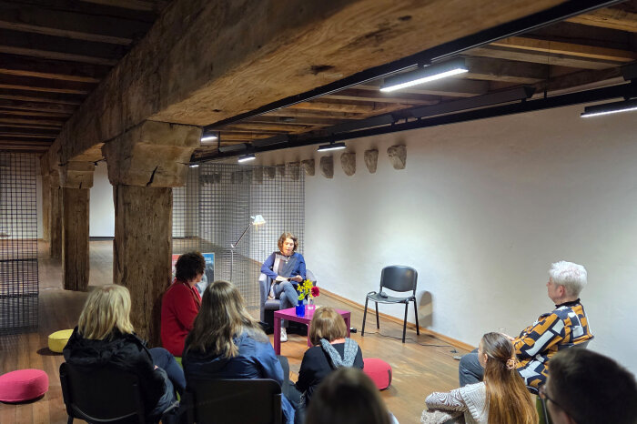 Eine Gruppe Menschen in einem rustikalen Raum mit bunten Kissen, Stühlen