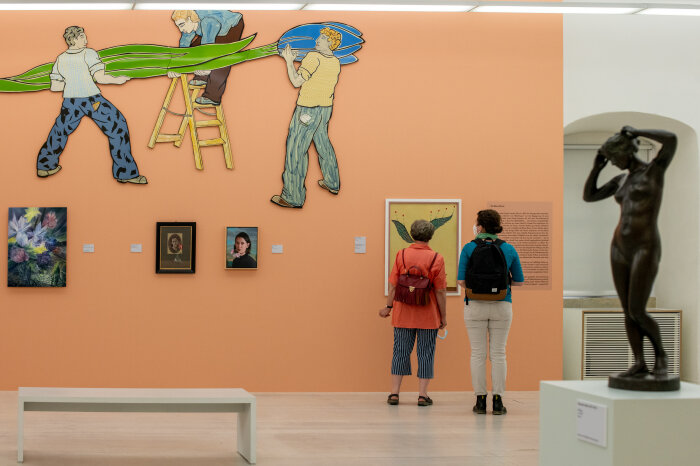 Zwei Frauen schauen sich eine Kunstausstellung mit Gemälden und Skulpturen an