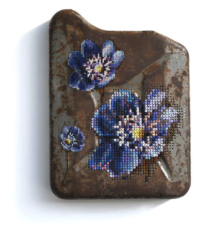 Ein rostiger Kanister bestickt mit drei Blumen in verschiedenen Blautönen.