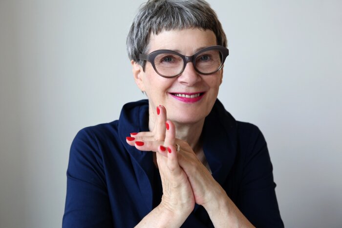 Eine Frau mit kurzen grauen Haaren und Brille in einem dunklen Oberteil