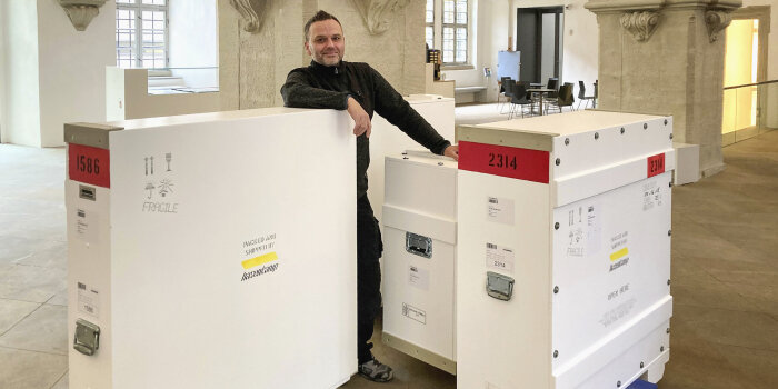 ein Mann steht neben großen weißen Kisten, die sich auf Rollwägen befinden