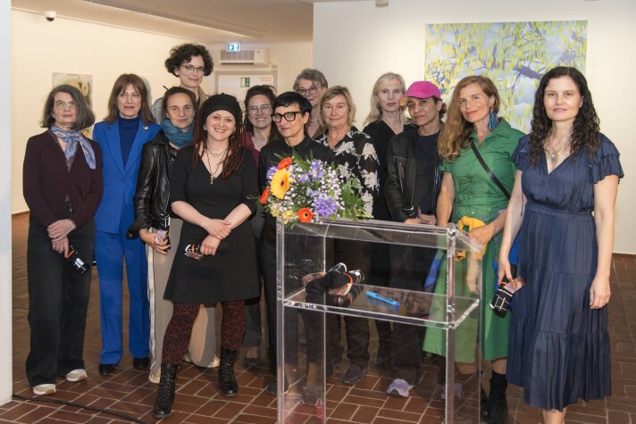 Mehrere Frauen stehen gruppiert und schauen in die Kamera, sie stehen in einem Raum mit Gemälden