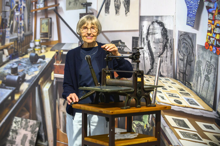 eine Frau steht an einer historischen Druckmaschine, im Hintergrund ein großformatiges Foto eines Ateliers