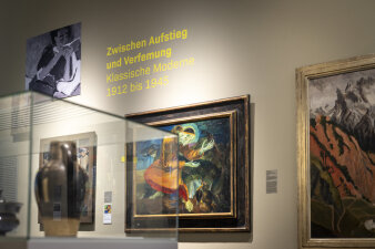 Wand mit Gemälden und Schriftzug "Zwischen Aufstieg und Verfemung" und Vitrine im Vordergrund