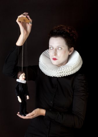 Eine Frau mit weißen Augen hält eine Marionette in der Hand
