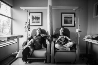 Schwarz Weiß Fotografie die einen Mann und eine Frau in einem Krankenhaus auf zwei Stühlen zeigt