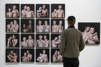 Ein Mann steht vor einer Wand mit Fotografien mit schwarzem Hintergrund und Männern mit nackten Oberkörpern