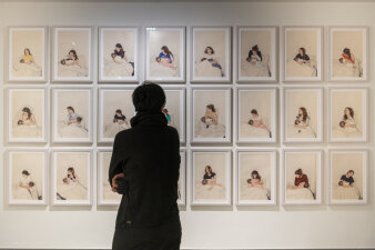 Drei Reihen mit gerahmten Fotos an einer Wand, davor eine Frau von hinten welche sich die Bilder anschaut