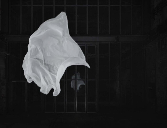 Fliegendes weißes Tuch vor dunkler vergitterter Wand