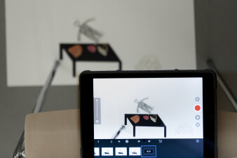 Ein Tablet welches gerade einen Film von einer Zeichnung einer Figur und einem Tisch aufnimmt.