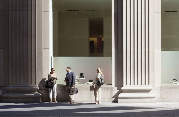 Fotografie einer Straßenszene mit drei Personen die vor einem Schaufenster und zwei großen Säulen stehen