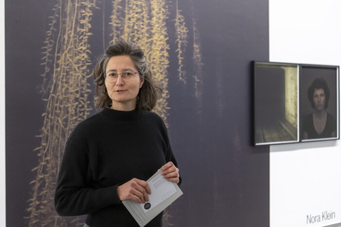 eine Frau in schwarzem Pullover vor einer Wand mit großformatigen Fotografien