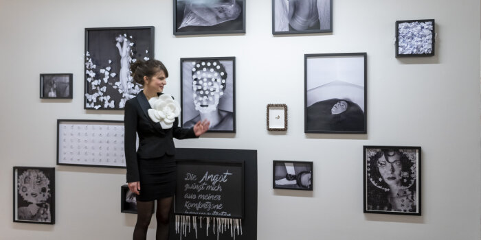 eine schwarz gekleidete Frau steht vor einer Wand mit Schwarz-Weiß-Fotografien
