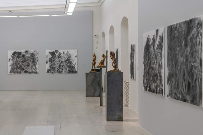 Ausstellungsraum mit Skulpturen und gerahmten schwarz-weißen Zeichnungen an den Wänden