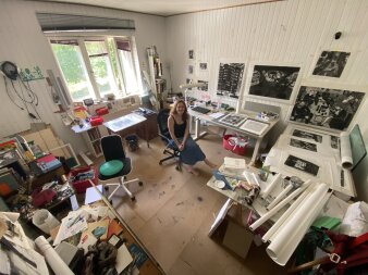 Eine junge Frau in einem bunten Kunstatelier mit Stühlen, Tischen und viel kreativem Material