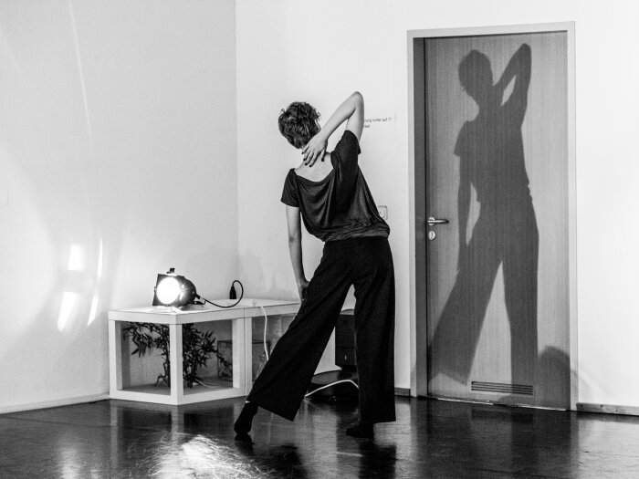 Ein Schwarz Weiß Foto einer Frau vor einer Tür stehend auf die ihr Schatten fällt.