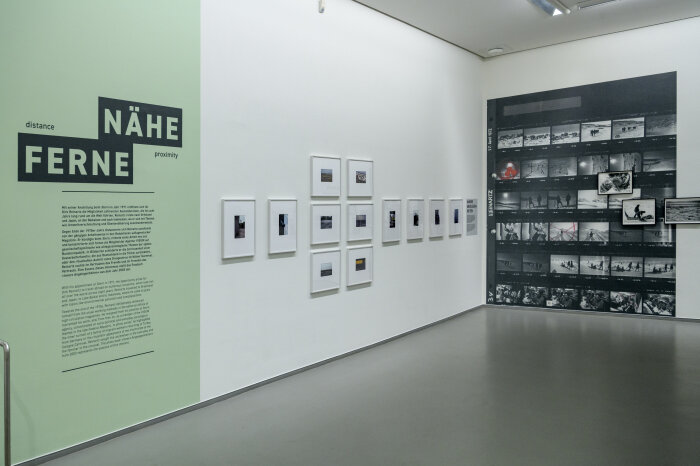 Blick in die Ausstellung „Dirk Reinartz. Fotografieren, was ist“ Eine grüne Wand mit Schrift, daneben verschiedene gerahmte Bilder
