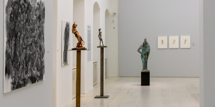 Ausstellungsraum mit Skulpturen und gerahmten Zeichnungen an den Wänden