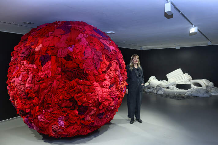 Eine Frau in einem dunklen Raum, links neben ihr ein großer Ball mit roten Stoffen