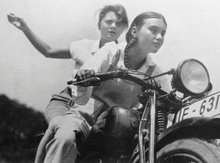 Schwarz-Weiß-Fotografie von zwei jungen Frauen die auf einem Motorrad sitzen