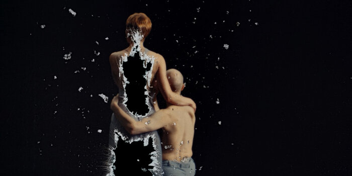 Eine stehende Person die sich aufzulösen scheint, daneben eine zweite Person sitzend