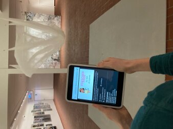 Smartphone in den Händen im Ausstellungsraum zeigt das Eröffnungsbild "Forschertour"