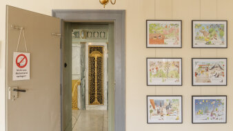 Eine Tür mit Schild, daneben verschiedene bunte Bilder an der Wand