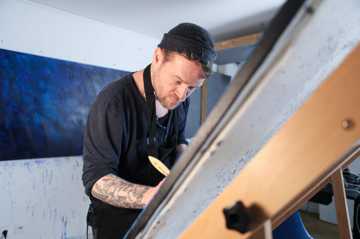 Portrait eines Mannes mit Mütze der stehend an einem Zeichentisch malt